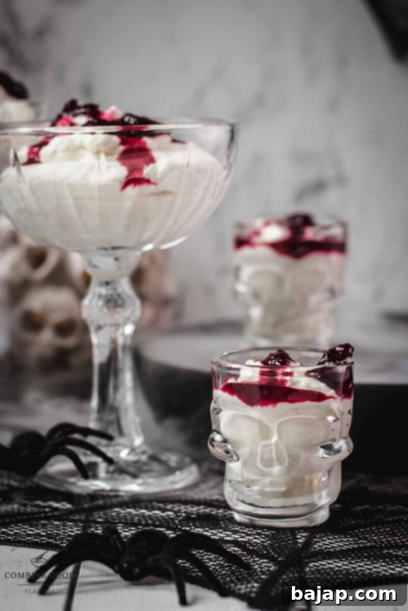 Spooky blood clot berry brains mousse, served in skull shaped shot glasses. A single skull-shaped glass of blood clot berry brains mousse is shown, garnished with more berry syrup dripping down the sides. The background is dark, highlighting the eerie dessert.