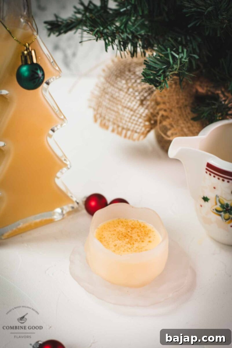 Delicious eggnog in a small icy bowl next to a Christmas tree shaped bottle, filled with eggnog.