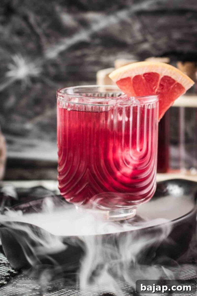 A spooky Bloody Sea Breeze cocktail, layered with red syrup at the bottom and a lighter red drink on top, garnished with a grapefruit slice, served in a tall glass.