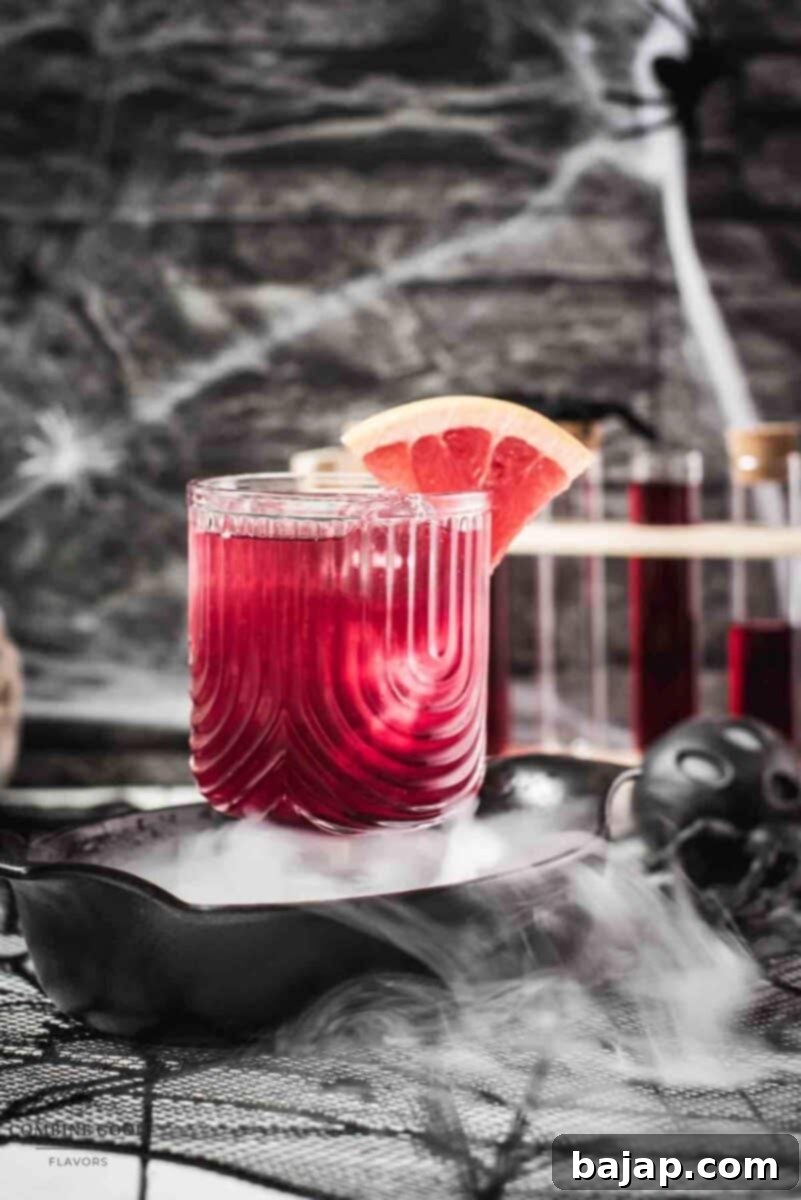 Ingredients and equipment needed to make the Bloody Sea Breeze cocktail, including glasses, jigger, citrus, and a bottle of Berry Blood Syrup.