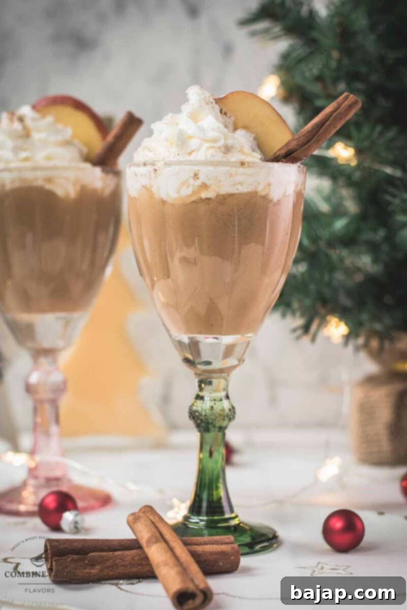 Decadent apple cider eggnog, garnished with a cinnamon stick, whipped cream, and apple slices.