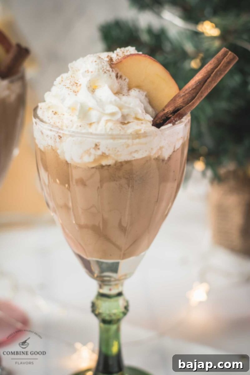 Decadent apple cider eggnog, garnished with a cinnamon stick, whipped cream, and apple slices.