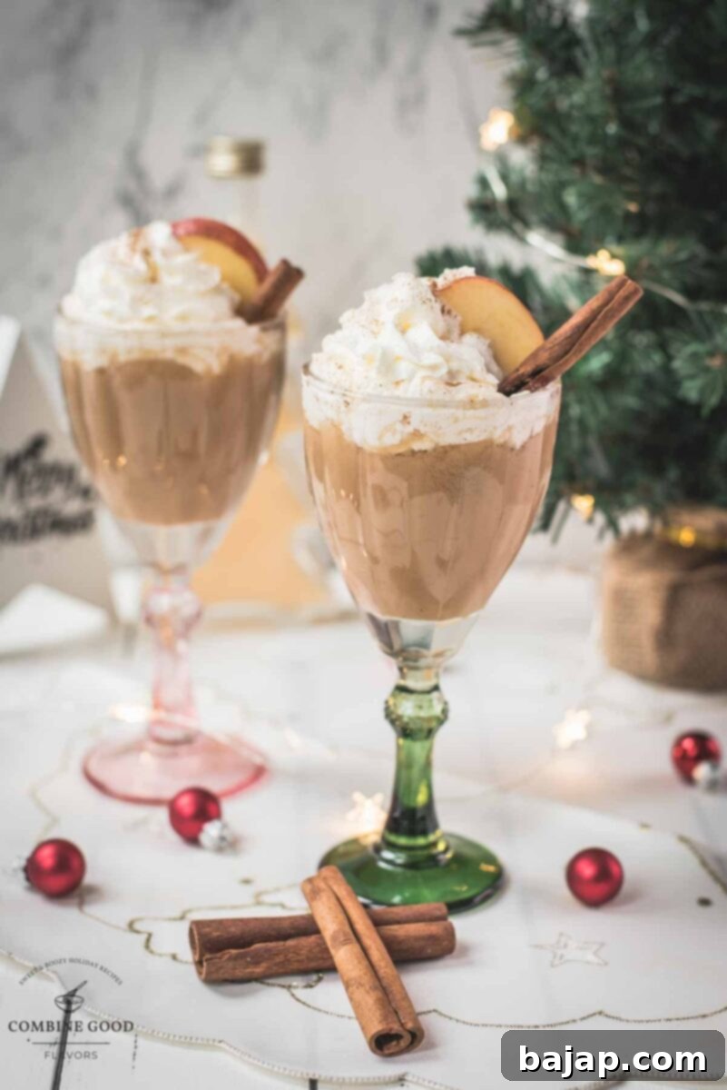 Decadent apple cider eggnog, garnished with a cinnamon stick, whipped cream, and apple slices.