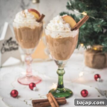 Decadent apple cider eggnog, garnished with a cinnamon stick, whipped cream, and apple slices.