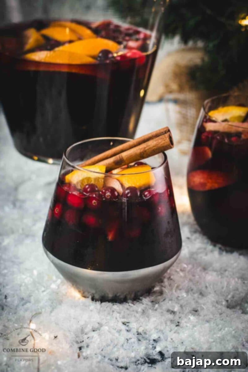 Gorgeous glass filled with delicious spiced winter sangria, garnished with a cinnamon stick. Placed on snow covered ground for a cozy holiday feel.