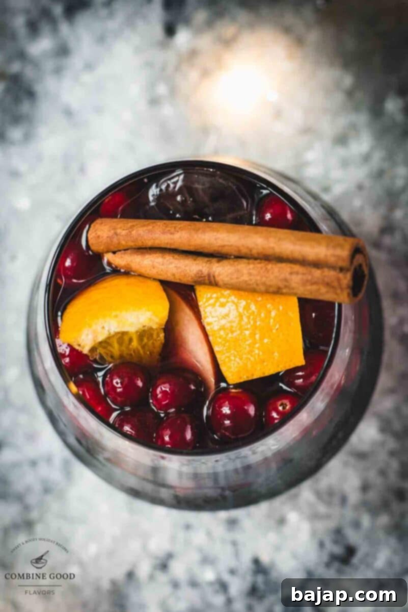 Beautiful glass of Spiced Winter Sangria, garnished with cinnamon and star anise, sitting on a snowy surface.