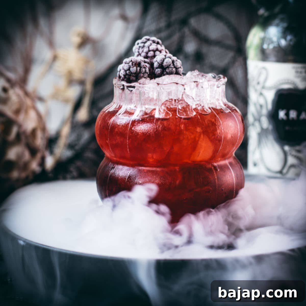 Spooky kramble cocktail, garnished with frozen blackberries and placed on a foggy plate.