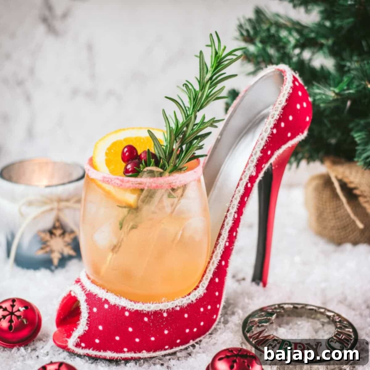 Festive vodka cranberry spritzer, garnished with rosemary twig, orange slice, and cranberries, served in a glass that is placed in a christmassy red high heel.