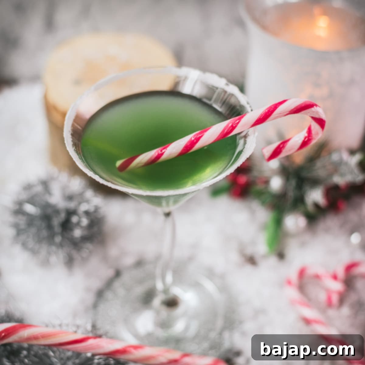 Festive cranberry peppermint martini in sugar rimmed martini glass. Garnished with a candy cane, placed on snowy ground.