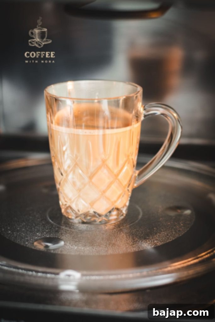 Glass mug filled with coffee and milk placed in microwave, illustrating the concept of reheating coffee.