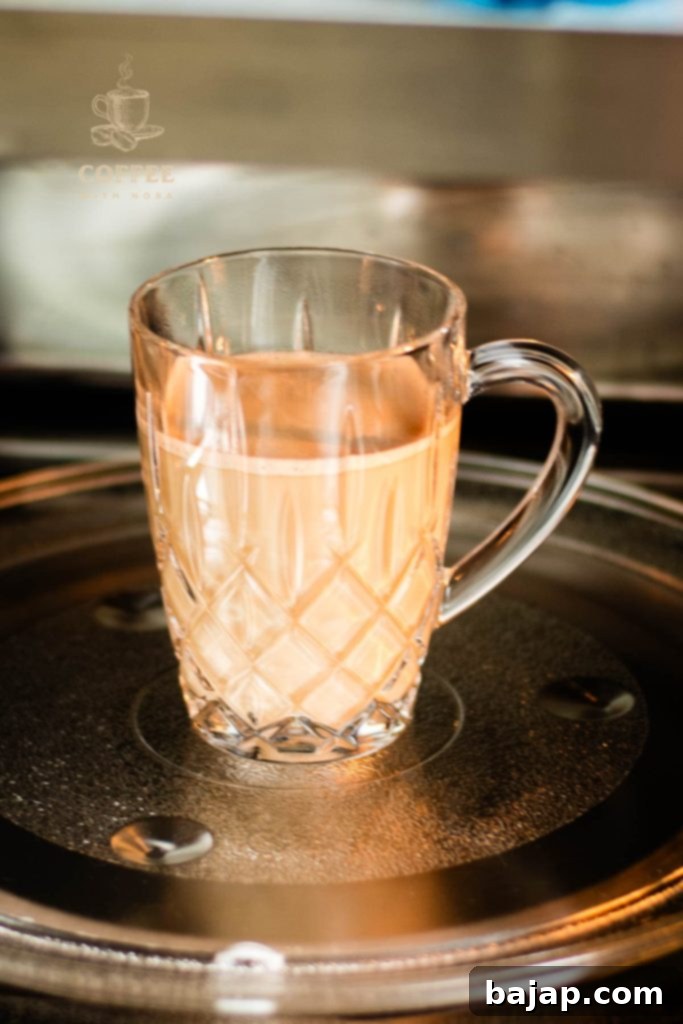 Glass mug filled with coffee and milk being placed in the microwave, demonstrating one method of reheating.
