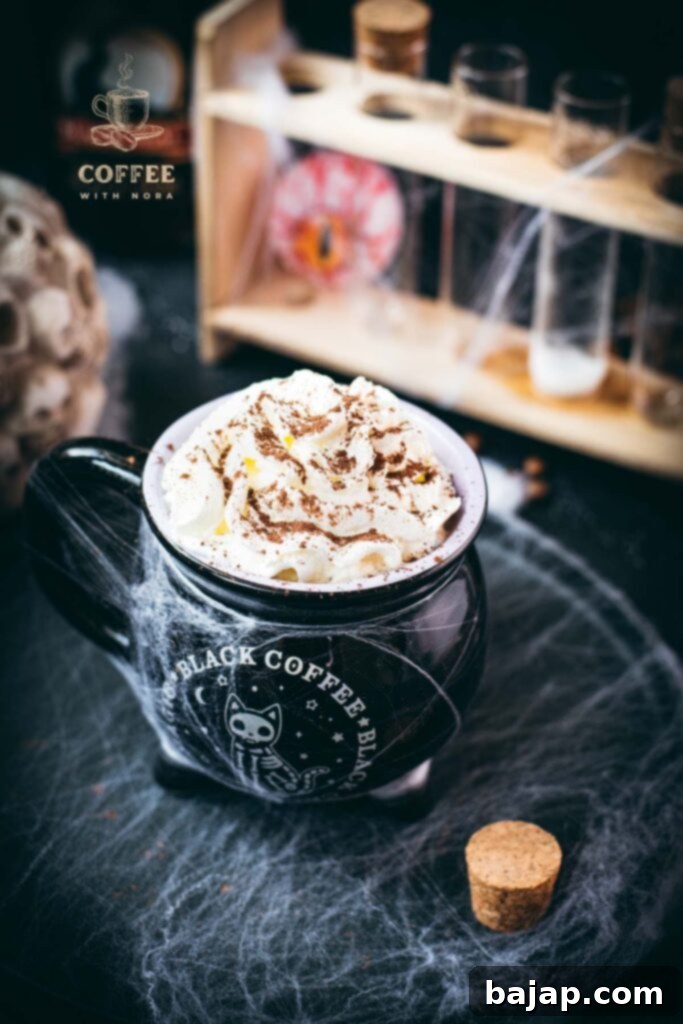 Spooky cauldron coffee mug filled with delicious coffee with rum. Topped with sweetened whipped cream and placed on a black plate surrounded by cobweb.