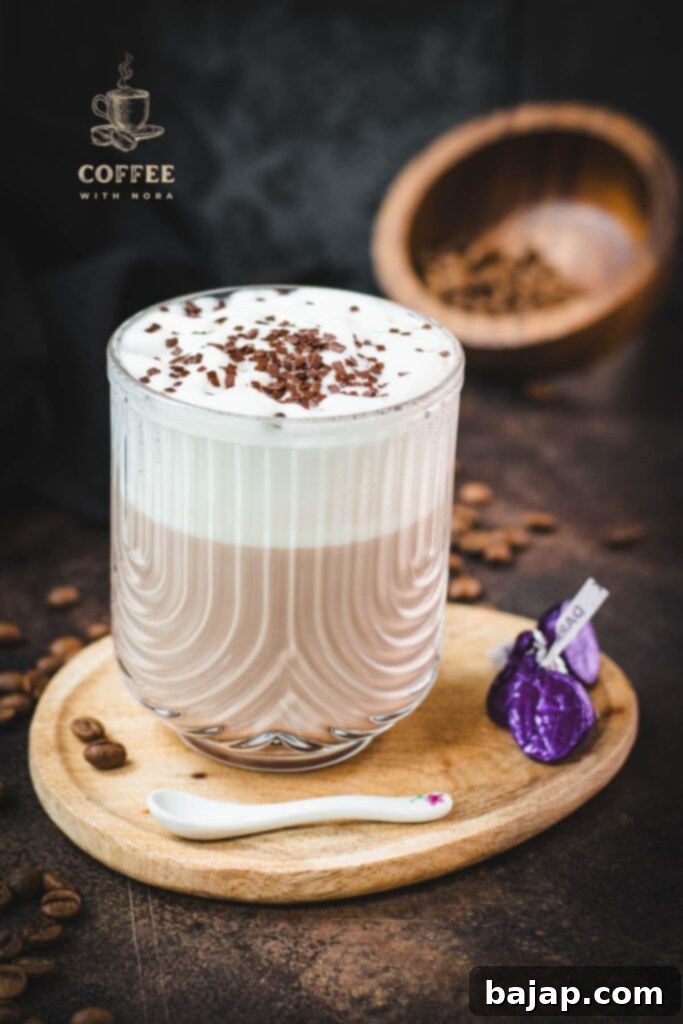 Finished mocha in a glass, topped with frothed milk and chocolate sprinkles, alongside dark chocolate pieces.