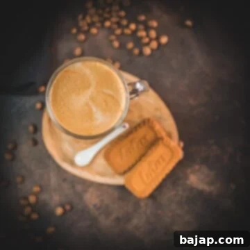 Super quick Biscoff Latte placed on small wooden plate next to two Biscoff cookies.